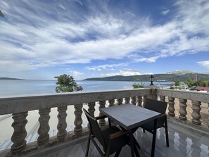 Een balkon met een tafel en stoelen, met uitzicht op een meer en bergen op de achtergrond.