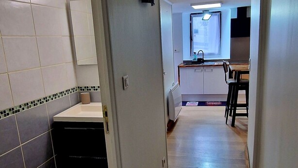 Un couloir menant à une cuisine et à une salle de bain, dont les murs sont recouverts de carreaux et le sol est en bois.