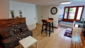 Un salon comprenant un canapé, une table à manger et des chaises. Il y a une horloge au mur et une fenêtre donnant sur l’extérieur.