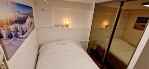 A small, compact room with two beds, a wall-mounted shelf with a lamp, and a large poster of a snowy mountain landscape. - Gîte de la Bégude Monts de Randon (Monts-de-Randon)