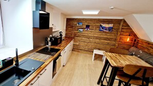 Une cuisine compacte avec une cuisinière moderne, un évier et un mur en bois orné de tableaux. On y trouve également un petit coin repas avec une table et des chaises.