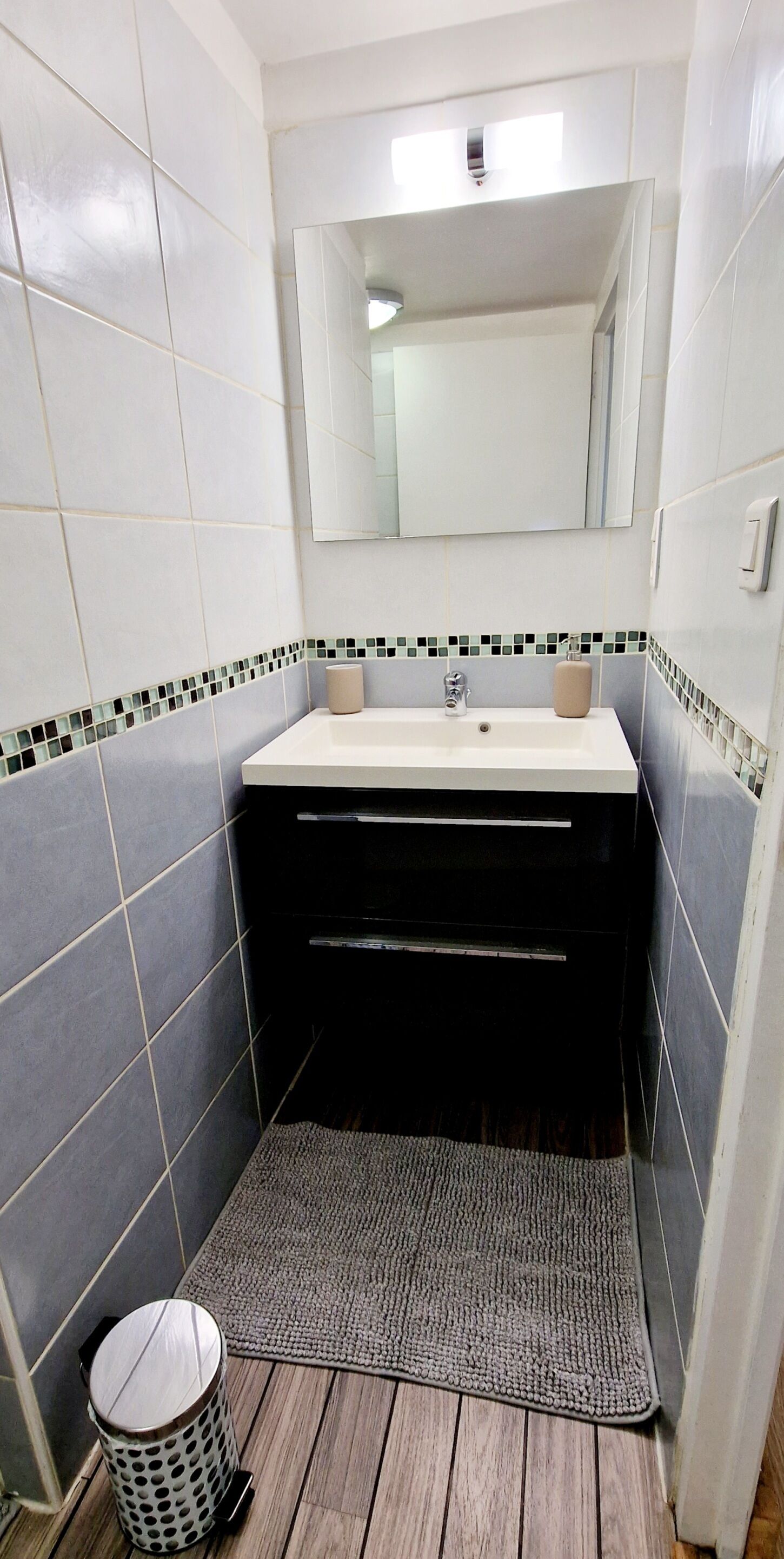 Une salle de bain avec un lavabo blanc, un miroir au-dessus et un sol carrelé.