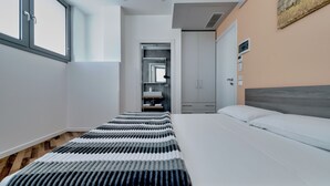 Une chambre d’hôtel moderne avec un grand lit, une armoire et une salle de bain visible à travers une porte ouverte.