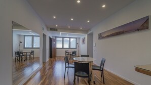 Une pièce spacieuse dotée d’un plancher en bois, d’une table ronde avec des chaises et d’une grande fenêtre laissant entrer la lumière naturelle.