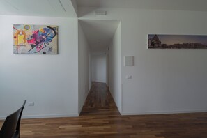 Un pasillo con piso de madera, una silla negra y dos obras de arte en las paredes.