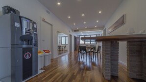 Un hall d’hôtel moderne comprenant une machine à café, un comptoir de réception et un espace repas avec des chaises et des tables.