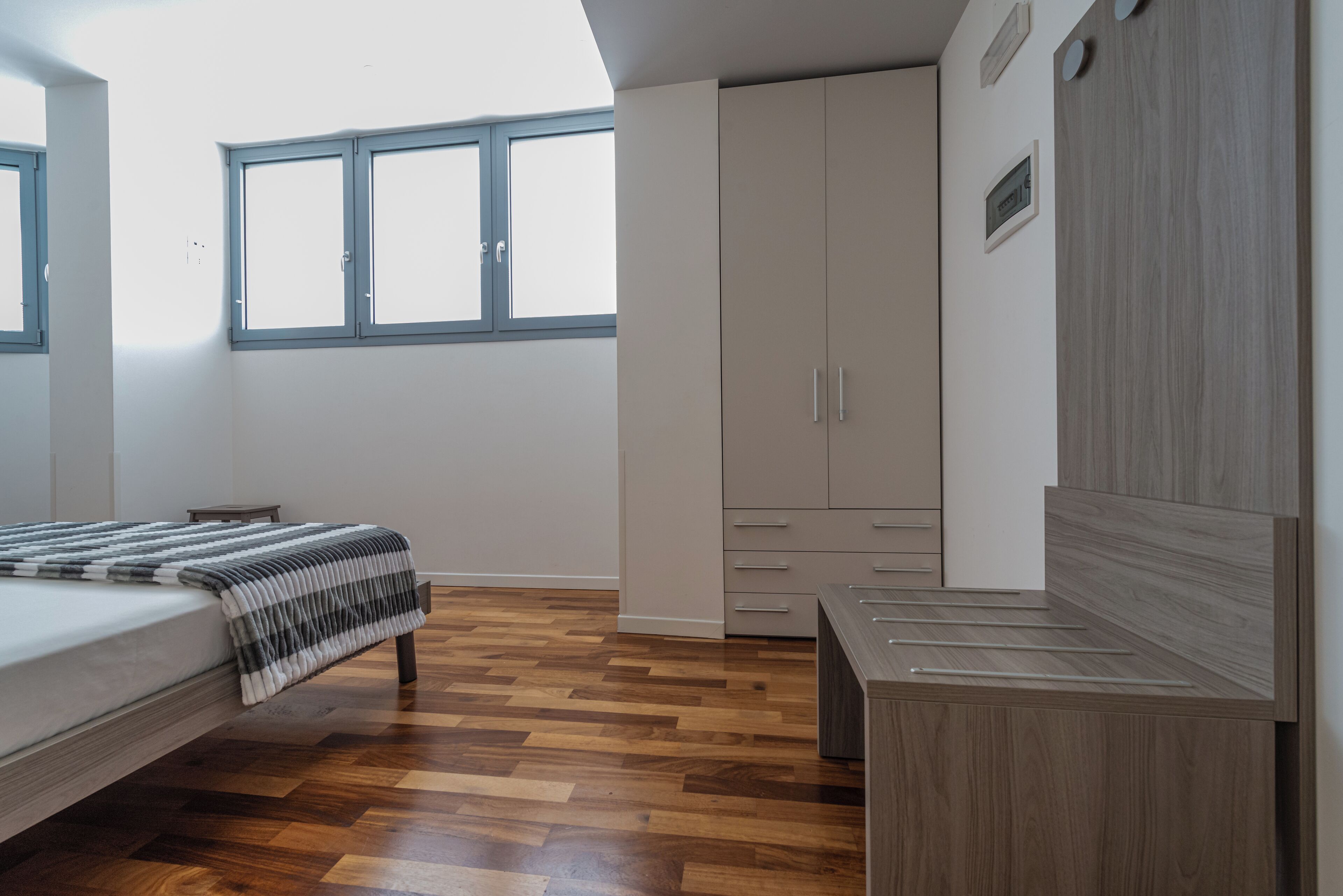 Quarto com cama, piso de madeira, guarda-roupa e escrivaninha.