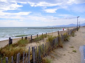 Una playa con una cerca de madera, una persona vestida de rojo y montañas al fondo.
