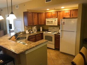 Una cocina con encimeras de granito, armarios de madera, estufa, microondas y refrigerador.