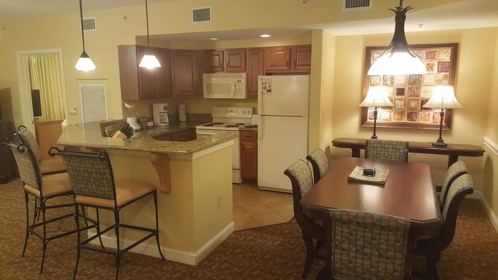 A kitchen with a central island, dining table, chairs, and a refrigerator.