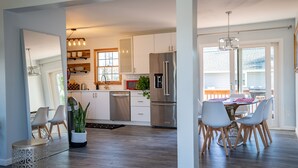 Une cuisine moderne avec des meubles blancs, des appareils en acier inoxydable et un coin repas comprenant une table et des chaises.