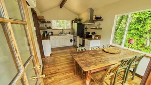 A kitchen with wooden flooring, a dining table with chairs, and a large window with a view of greenery. - Rivers Breeze - Wine Tastings Included (Healdsburg)
