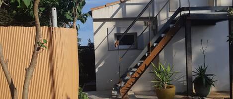 A residential building with a staircase leading to an upper floor, a bamboo fence, and potted plants.