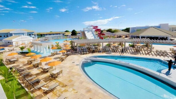 Ein Resort mit großem Pool, Liegestühlen, Sonnenschirmen und einer Wasserrutsche.