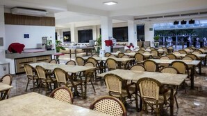 Ein großzügiges Restaurant mit mehreren Tischen und Stühlen, einer Theke mit rotem Tuch und Blick ins Freie durch große Fenster.