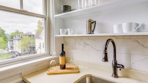 A kitchen with a window, a sink, and shelves with dishes and a wine bottle. - Beautiful Providence Apt Near Dtwn & Federal Hill! (Providence)