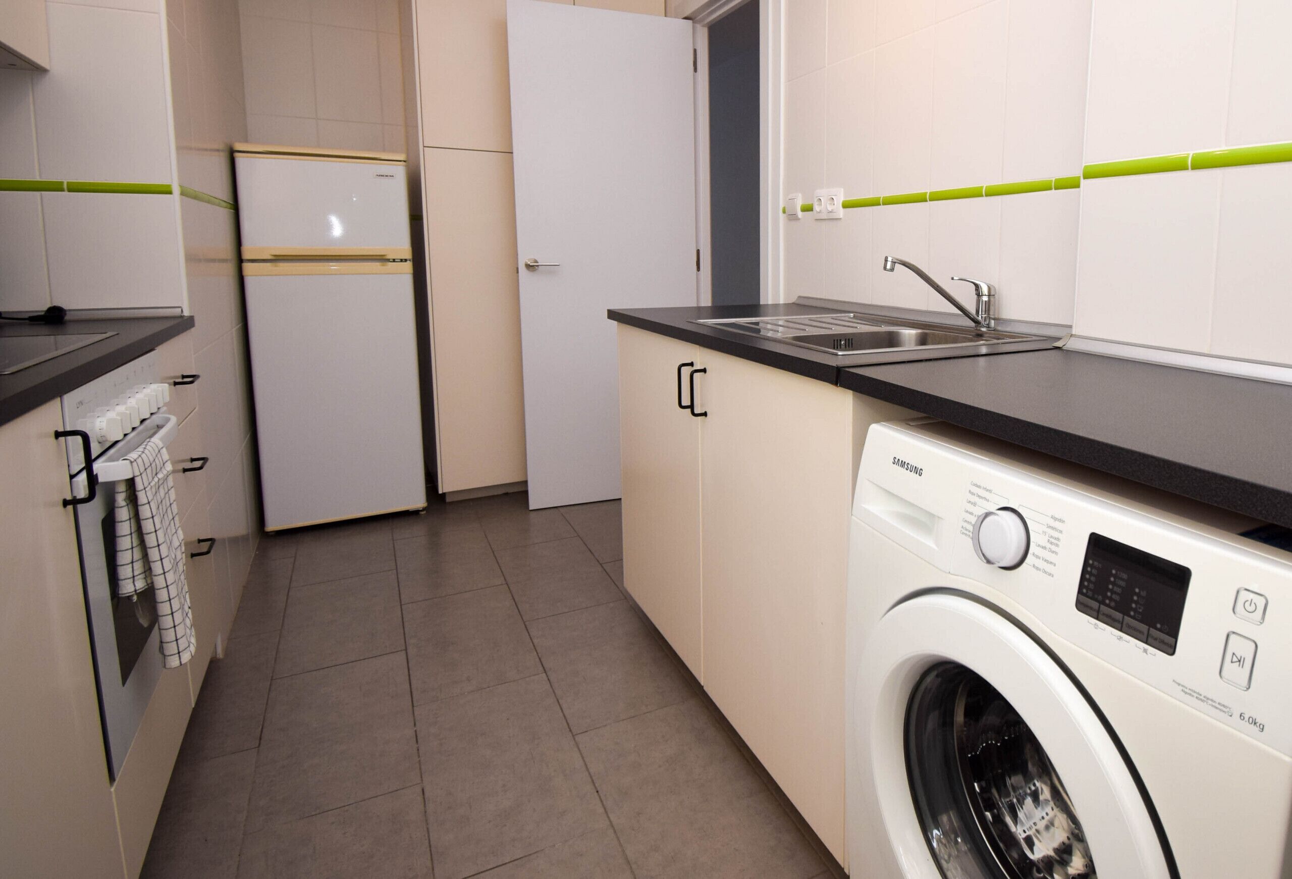 Une cuisine compacte équipée d’un lave-linge, d’un réfrigérateur et d’un évier.