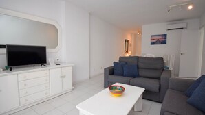Ein modernes Wohnzimmer mit einem Flachbildfernseher, einem weißen Tisch und zwei grauen Sofas mit blauen Kissen.