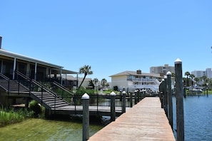 A wooden pier extending into a body of water, with a bridge connecting to a building with balconies. - Coral Cove 2001 (Destin)