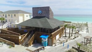 Un edificio frente a la playa con techo inclinado, una escalera que lleva a un nivel superior y vistas a la playa.