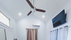 Ein Schlafzimmer mit Bett, Deckenventilator, Klimaanlage, Fernseher und Vorhängen.