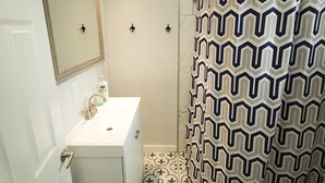 Ein Badezimmer mit einem weißen Waschbecken, einem Spiegel, einer Dusche mit gemustertem Vorhang und einer Toilette.
