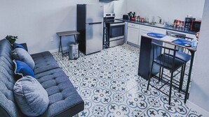Eine kompakte Küche mit modernen Geräten, ein Essbereich mit Barhocker und eine Couch mit Zierkissen.