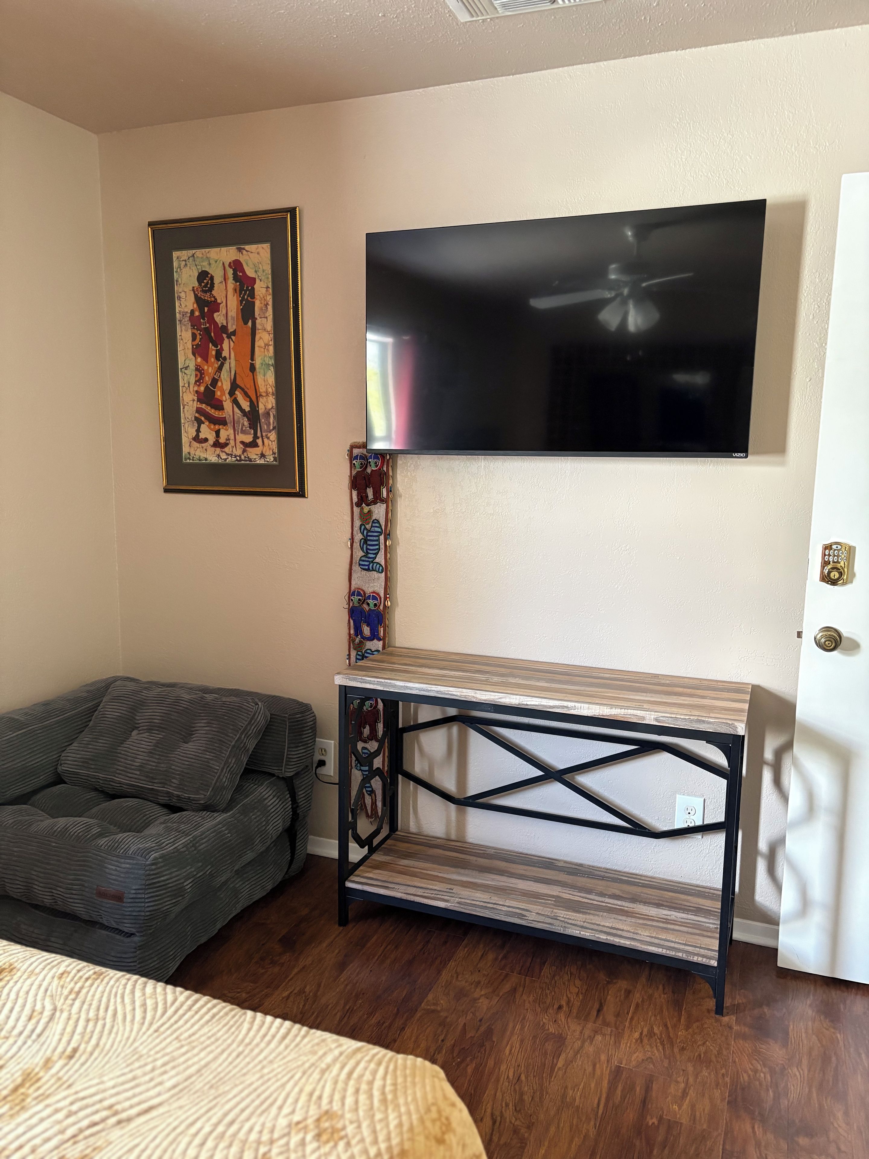 A room with a bed, a sofa, a TV mounted on the wall, and a small table with a decorative item on it.