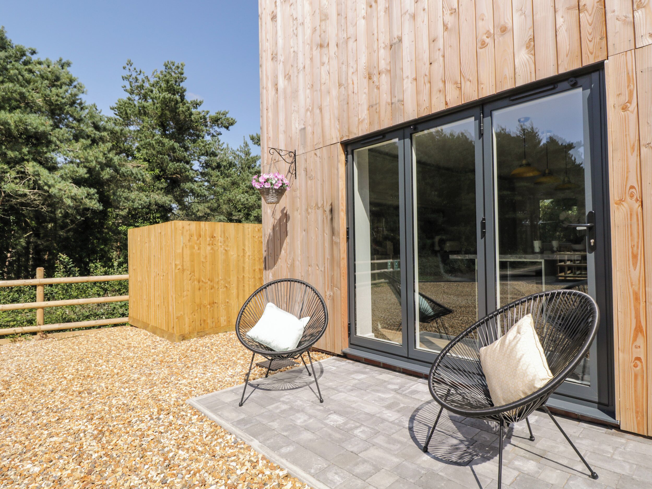 A wooden building with large glass doors, two wicker chairs with cushions, and a wooden fence.