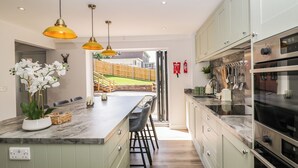 Cocina moderna con encimera de mármol, armarios verdes y una isla central con taburetes de bar. Se ve un patio trasero a través de una puerta abierta.