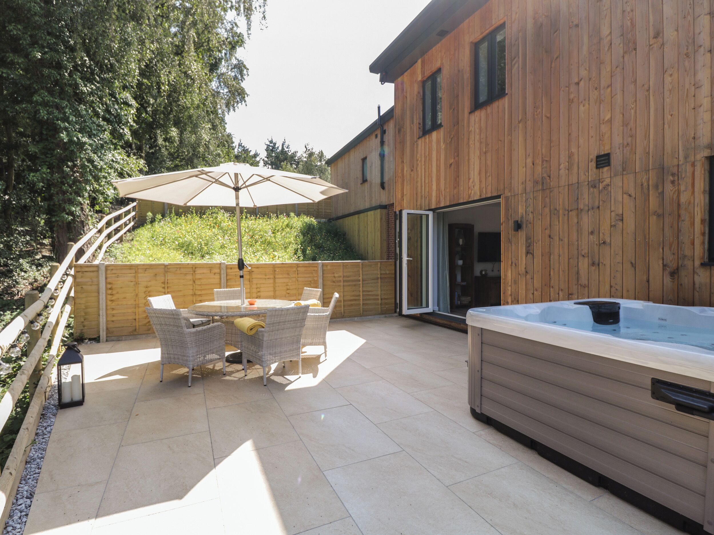 Un patio al aire libre con un jacuzzi, sillas de mimbre y una mesa con sombrilla.