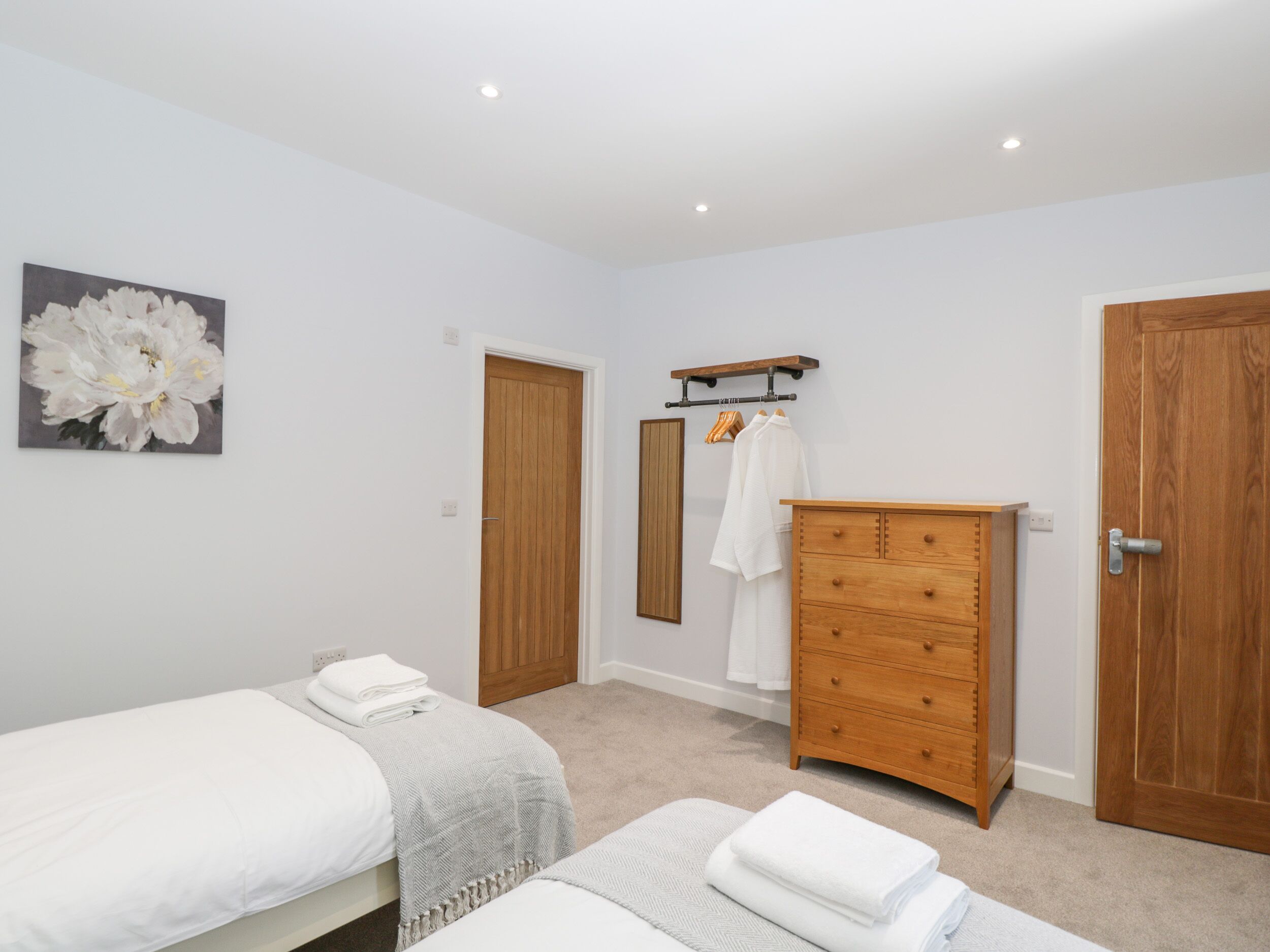 A bedroom with two beds, a wooden dresser, a mirror, and a wall-mounted towel rack.