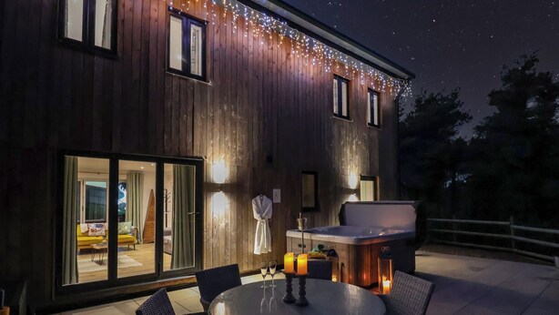 Un edificio moderno de madera con un patio que cuenta con una mesa redonda, sillas y un jacuzzi.