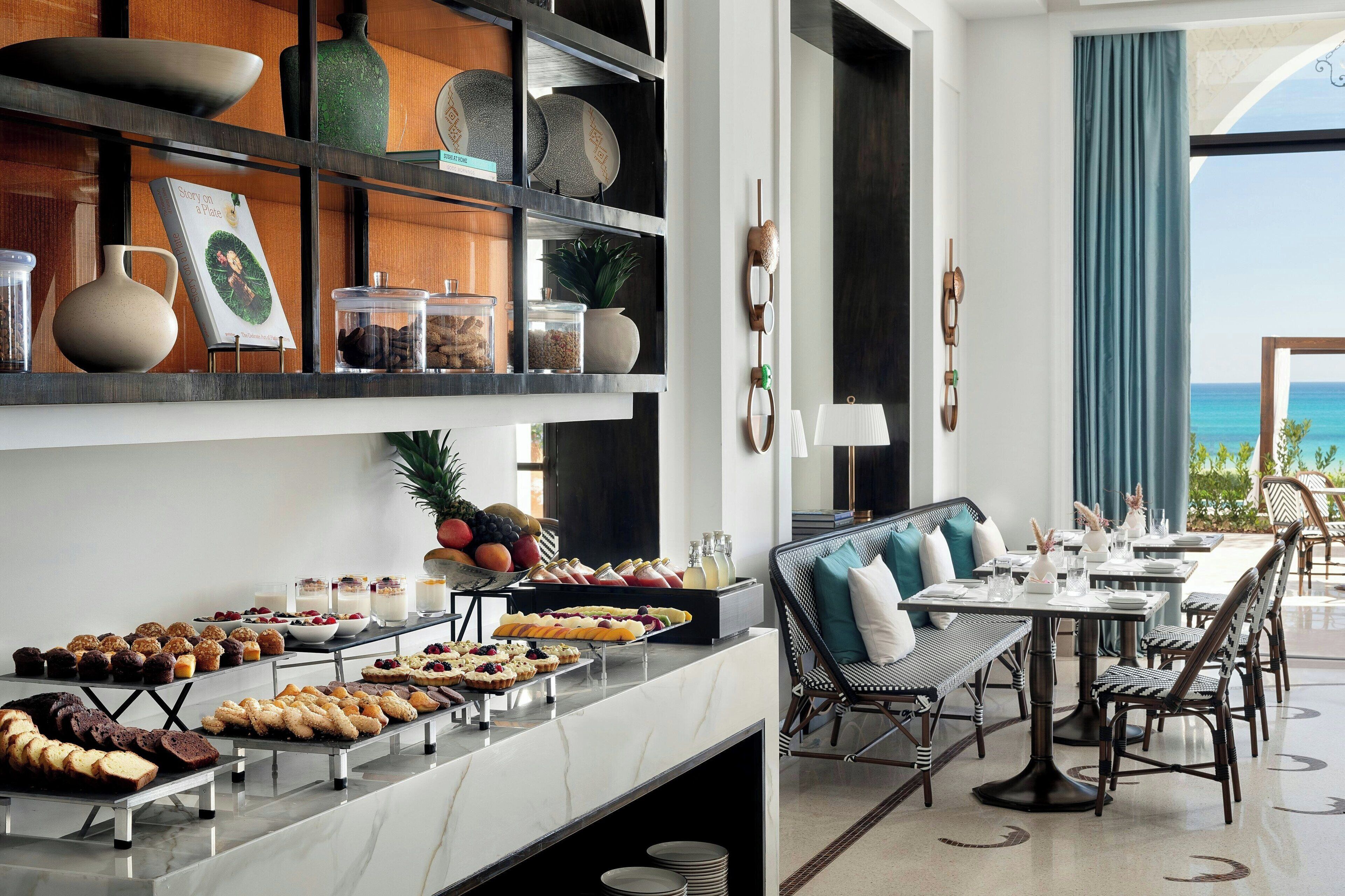 A buffet with various foods and drinks, a seating area with tables and chairs, and a view of the ocean.