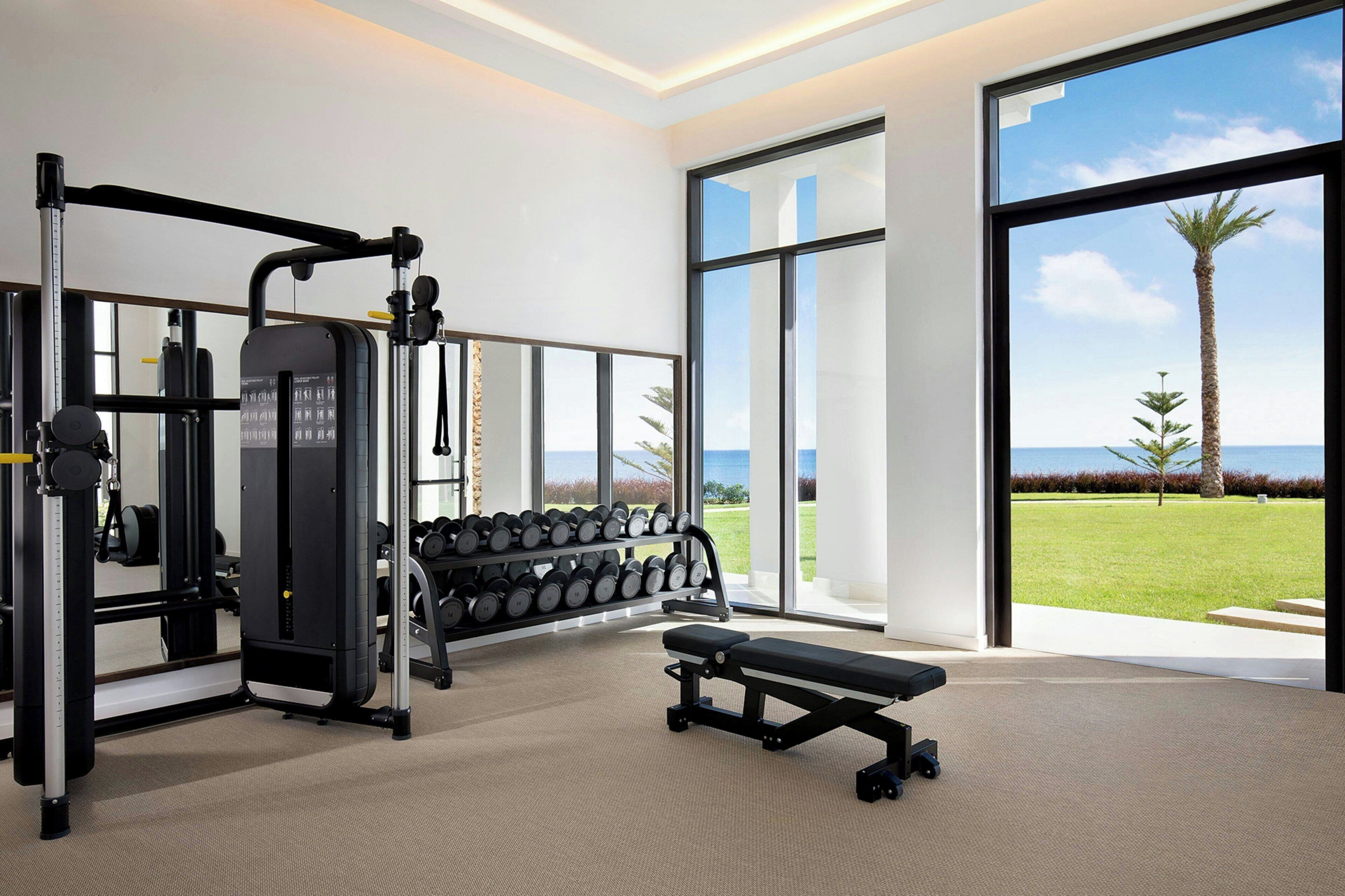 A gym with exercise equipment, a bench, and large windows offering a view of the outdoors.