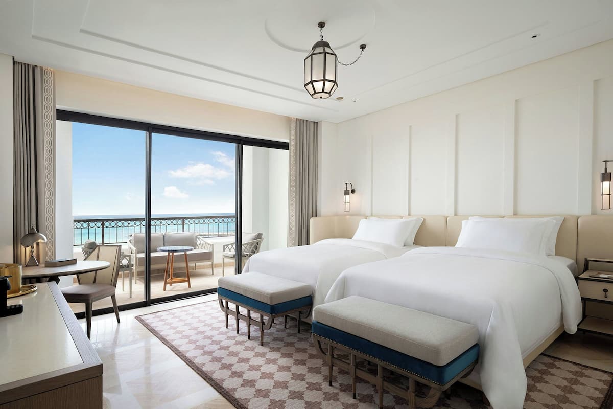 Une chambre d’hôtel avec deux lits, un bureau et un balcon donnant sur la mer.