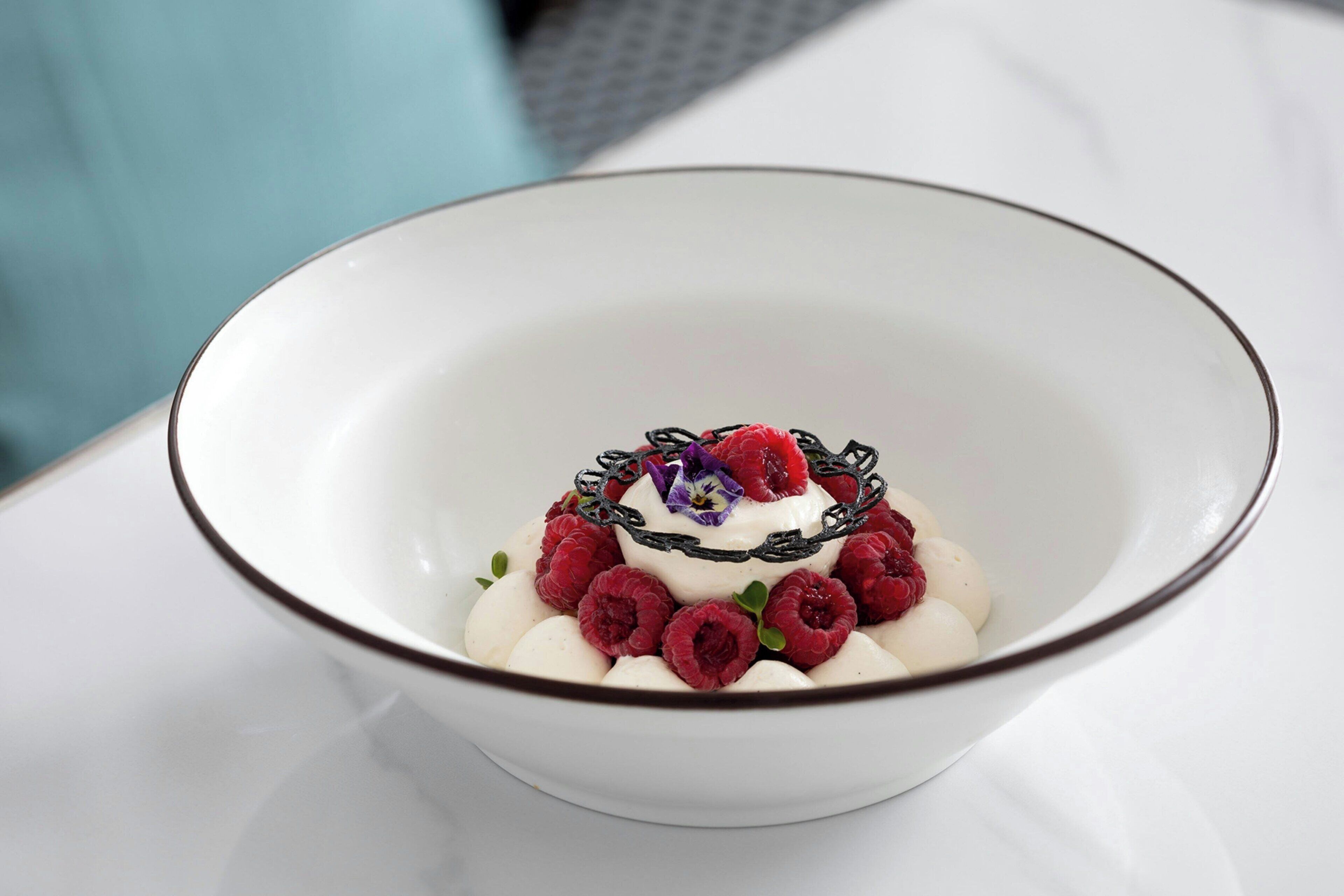 Un bol blanc à bordure marron contenant des objets sphériques blancs, des baies rouges et une fleur violette.