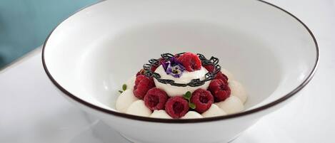 Un bol blanc à bordure marron contenant des objets sphériques blancs, des baies rouges et une fleur violette.