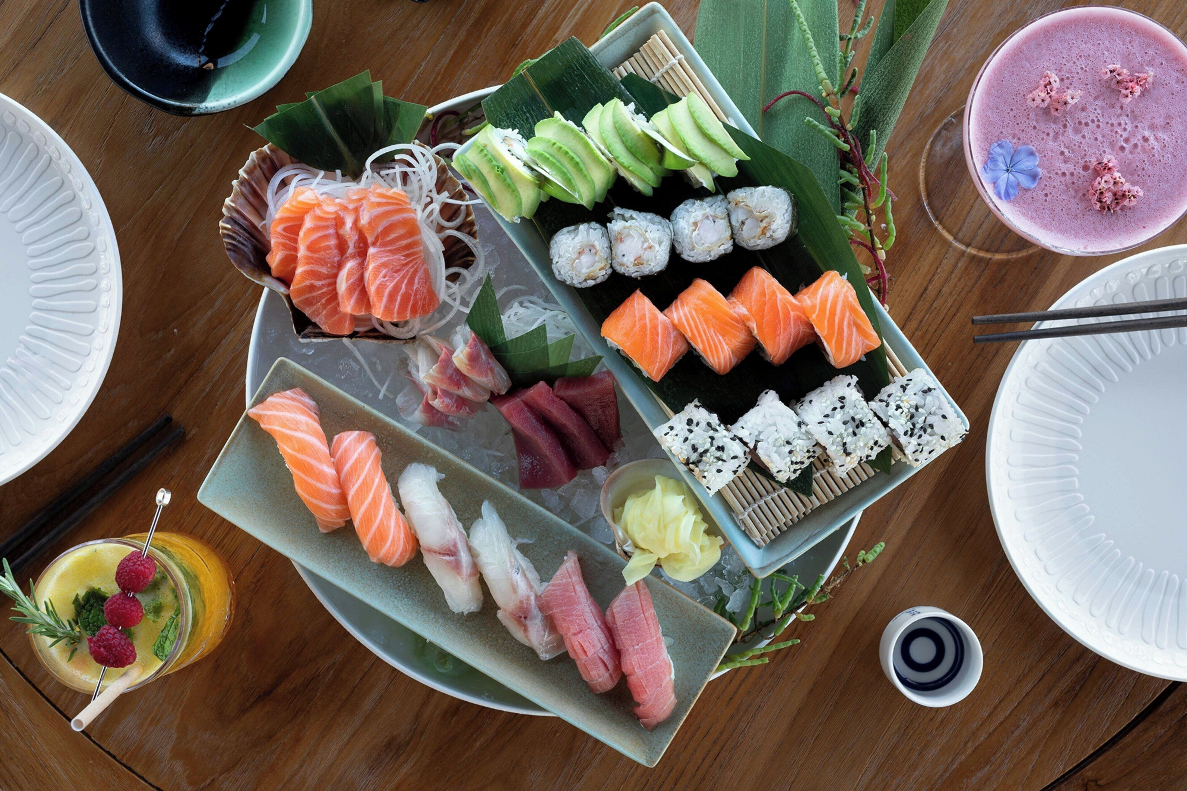A sushi platter with various types of sushi and sashimi, a glass of drink, and a bowl of soup.