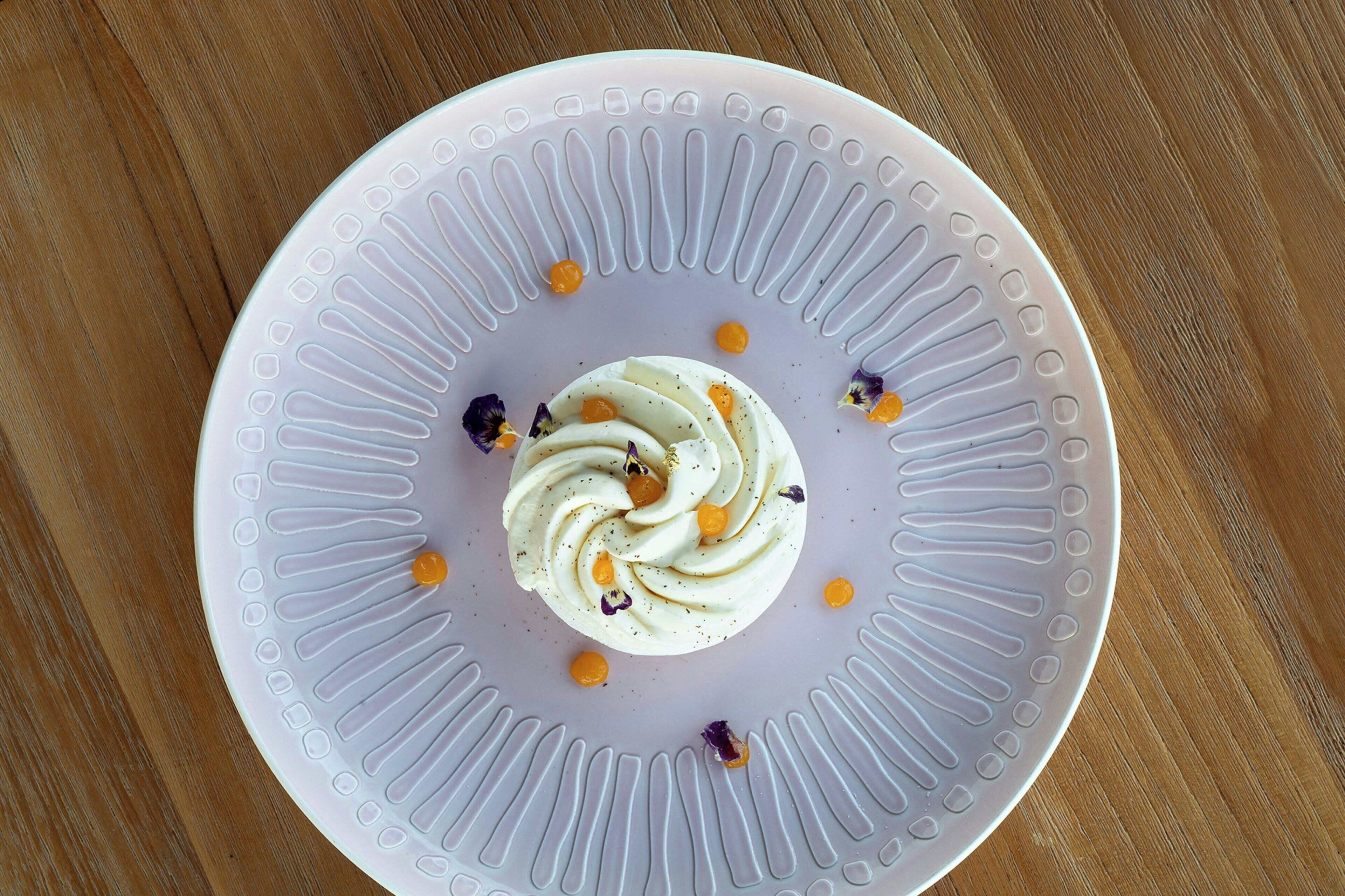 A white plate with a swirl of white cream and orange dots on a wooden table.