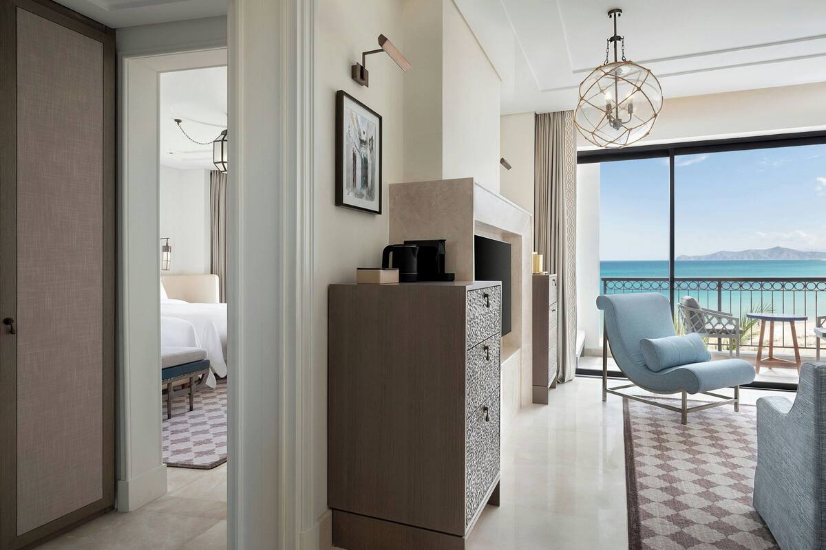 Une chambre d’hôtel avec une grande fenêtre, un canapé, un fauteuil, une télévision et un mini-bar.