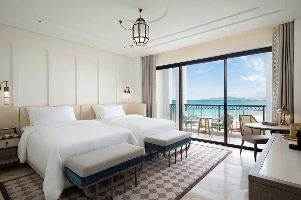 Une chambre d’hôtel avec deux lits, un balcon avec une table et des chaises, et une vue sur la mer.