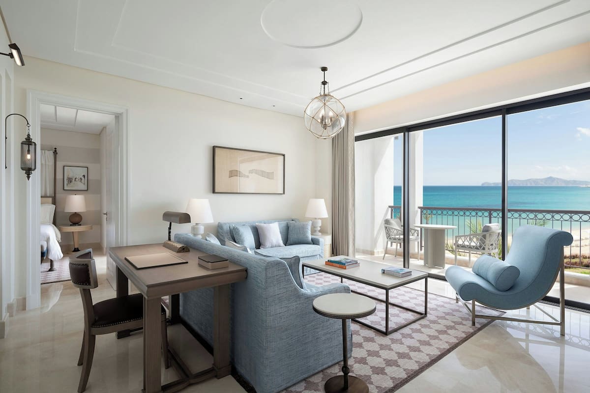 Une chambre d’hôtel moderne dotée d’un grand balcon, d’un canapé, d’une table à manger et offrant une vue sur la mer.