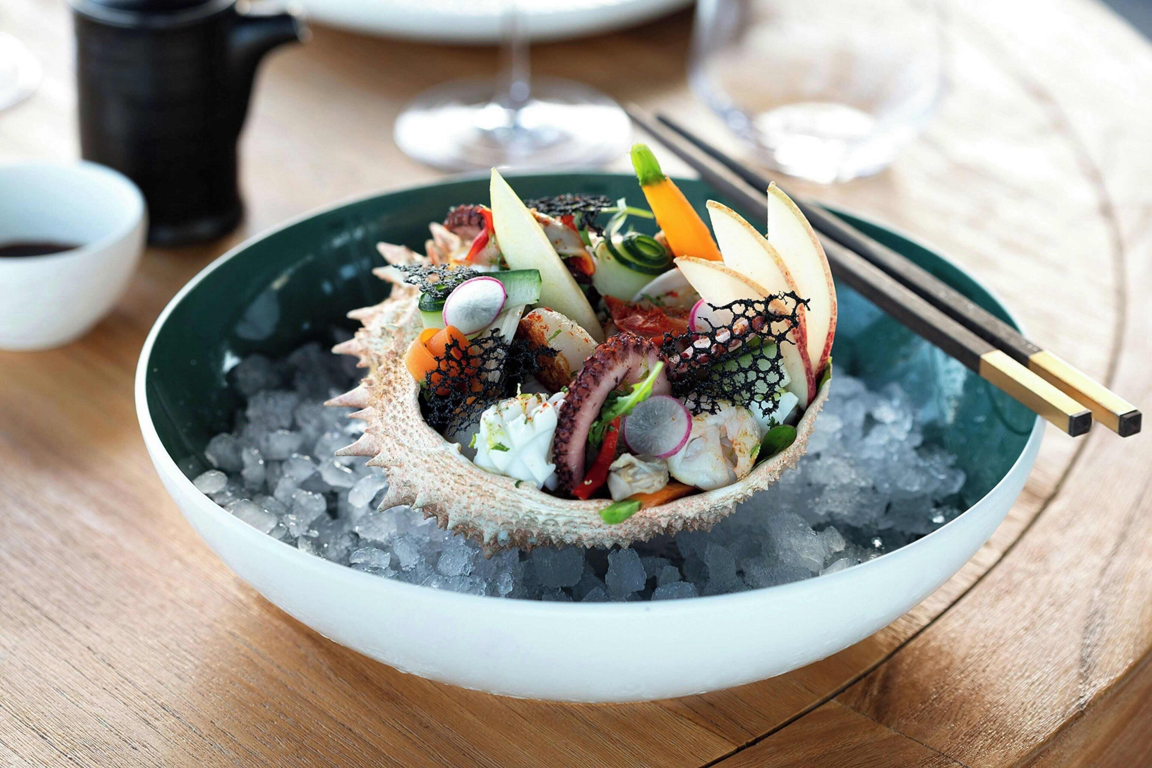 Un bol de salade de fruits de mer servie sur de la glace, accompagné de baguettes.