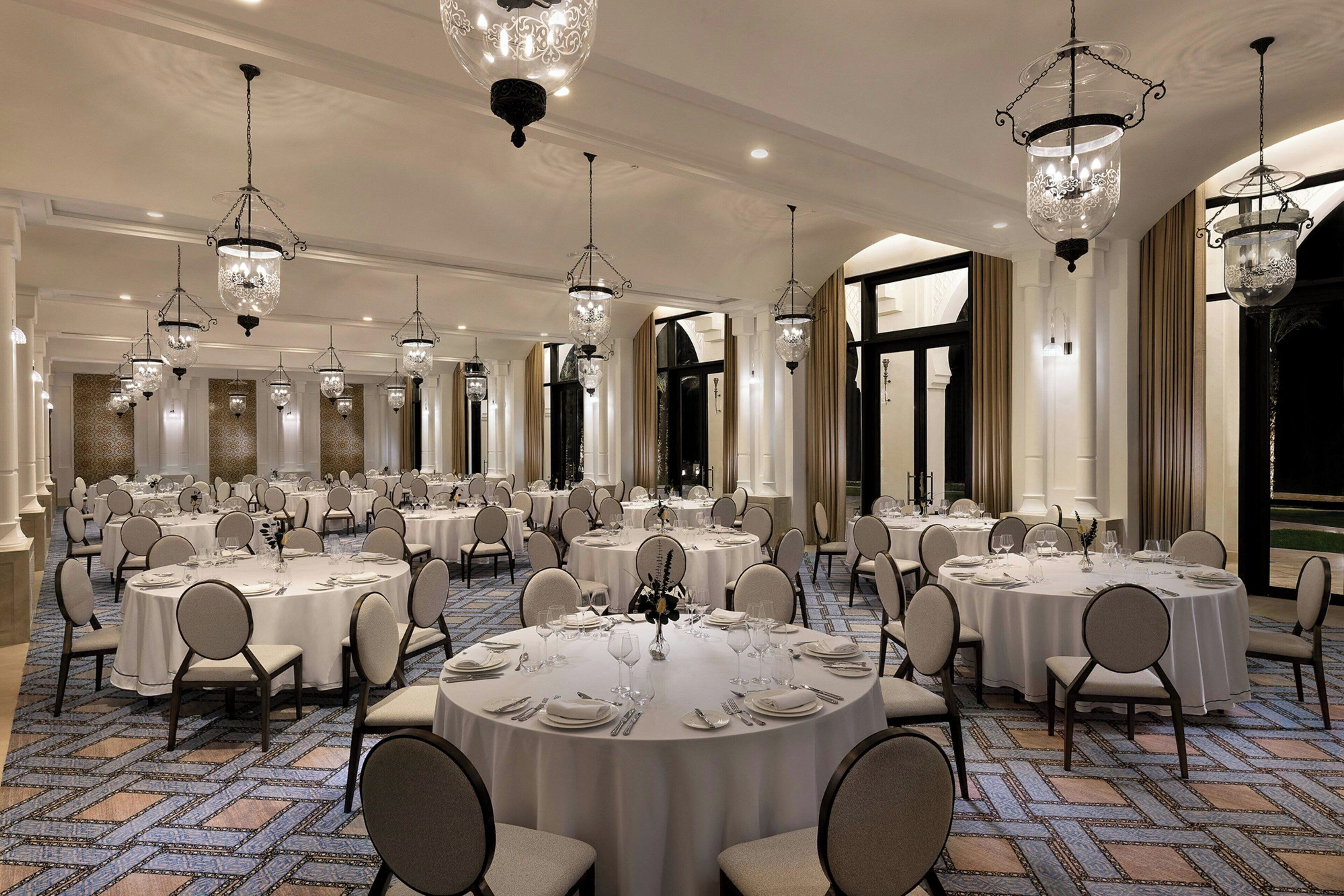 Une salle de banquet avec des tables rondes dressées pour le repas, des lustres et un sol recouvert de moquette.