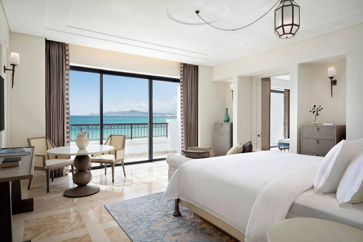 Une chambre d’hôtel avec un grand lit, un bureau avec des chaises, une vue sur la mer et un balcon.