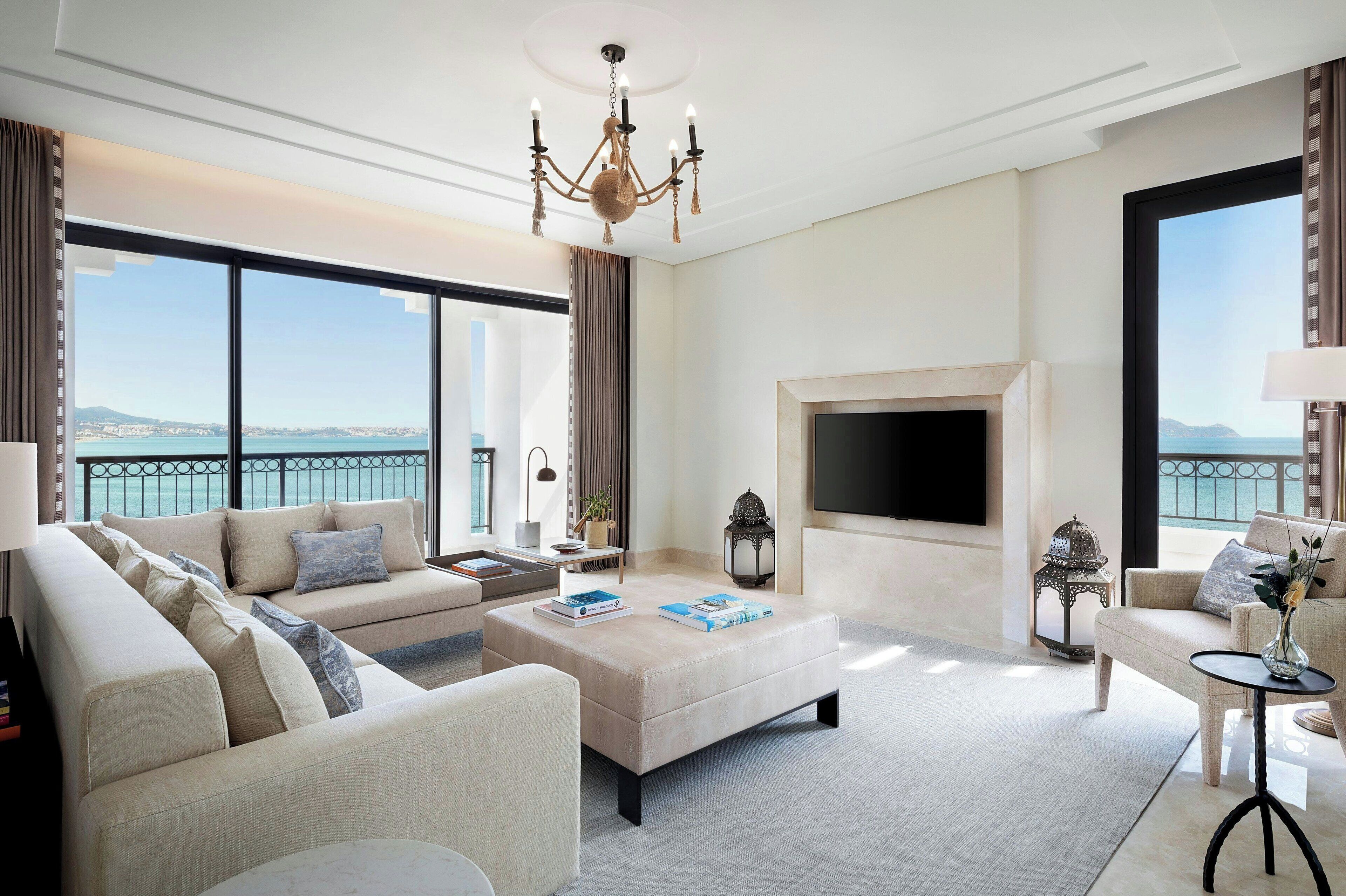 Un salón amplio con un sofá grande, una mesa de centro y una chimenea. Una ventana grande ofrece vistas al mar.