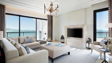 Un salón amplio con un sofá grande, una mesa de centro y una chimenea. Una ventana grande ofrece vistas al mar.