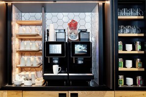 A coffee machine with two screens, a basket of utensils, and a cup on the counter. - Moxy Vienna City East (Vienna)
