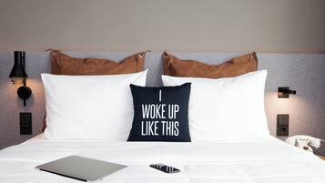 A neatly made bed with a laptop and a smartphone on it, a pillow with the text "I woke up like this," and a telephone on the side.